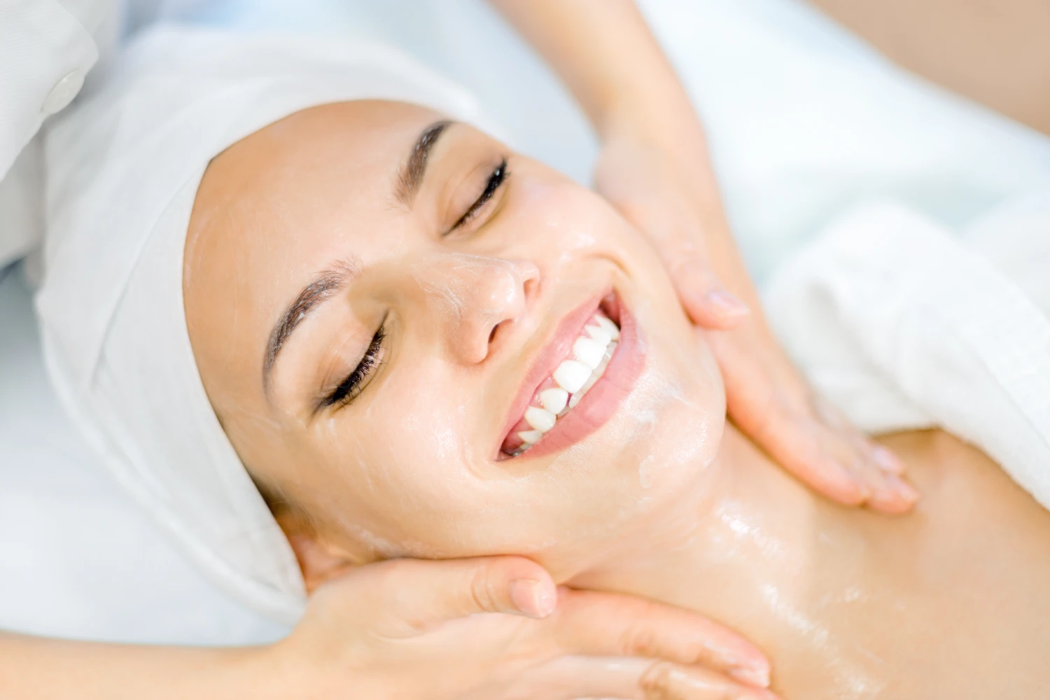 Kosmetologie. Die Hände einer Kosmetikerin führen eine Gesichtsmassage mit einer Maske durch. Lächelndes Mädchen bei einer Spa-Behandlung.